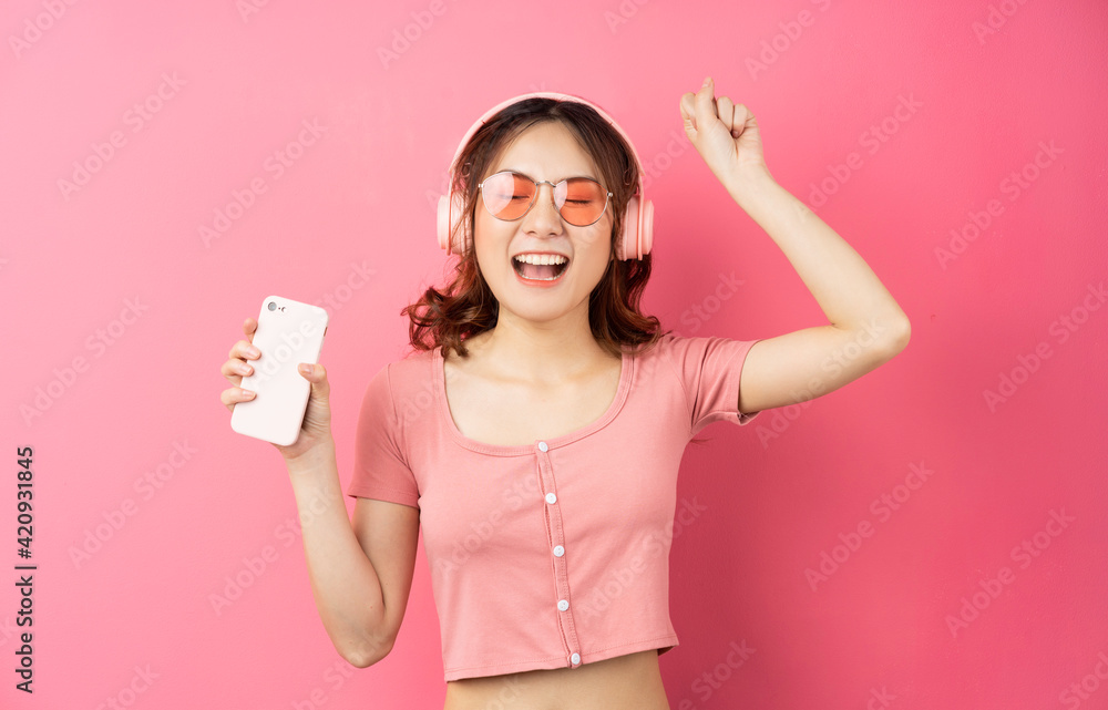Young asian girl wearing headphones and using the phone on pink background Young asian girl wearing headphones and using the phone on pink background