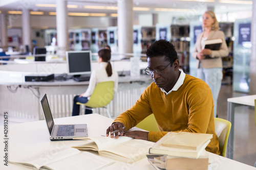 Confident african-american man working on laptop in public library. High quality photo