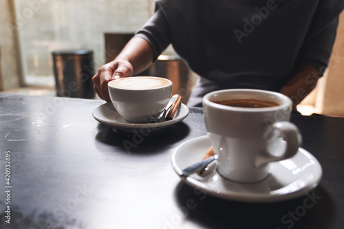 Closeup image of a woman holding a white cup of coffee on the table to drink in cafe