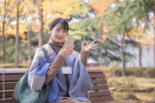 秋の公園でスマホを使う会社員の女性 