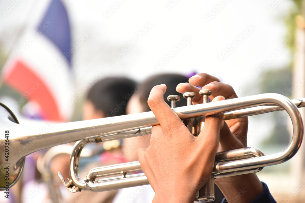 Obraz premium Trumpet instrument holding in hands of Asian student who playing it at a ceremony to honor the national flag in the morning. Soft and selective focus on trumpet.