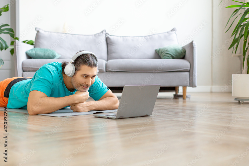 A middle aged man in headphones during an online video conversation. He lies on the floor in front of a laptop monitor A middle aged man in headphones during an online video conversation. He lies on the floor in front of a laptop monitor