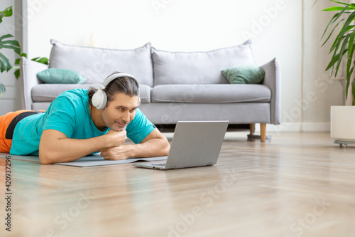 A middle aged man in headphones during an online video conversation. He lies on the floor in front of a laptop monitor