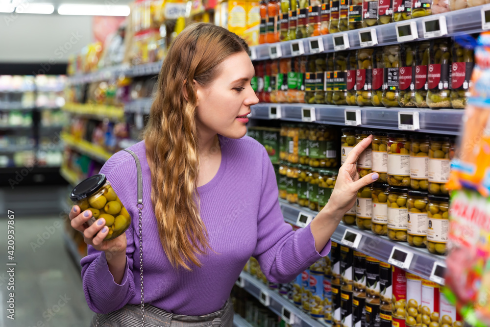 Woman choosing jar of preserved olives in the shop