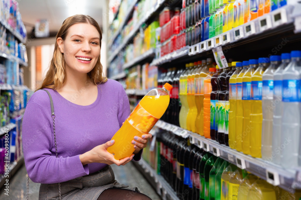 Portrait of young happy glad cheerful positive smiling woman satisfied with choosed carbonated soft drinks in food store