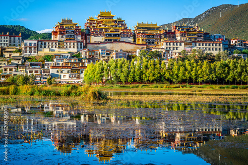 Beautiful scenic view of Ganden Sumtseling monastery with water reflection at sunset and blue sky Shangri-La Yunnan China