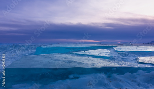 Ice hummocks of Lake Baikal close-up. Turquoise layers of ice under the evening sky with lilac clouds. Russia
