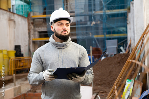 Young bearded foreman making task list during works in building under construction