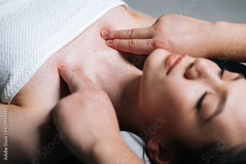 Close-up top view of young woman lying down on massage table with closed eyes during shoulder and neck massage at spa salon. Male masseur professionally massaging shoulders on black background.