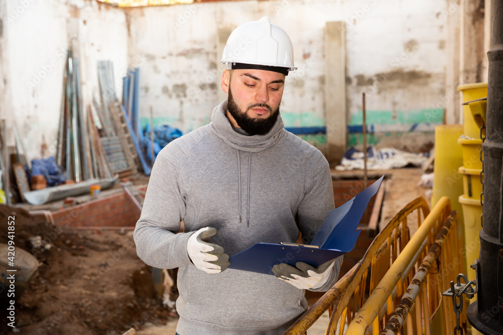 Fototapeta premium Young bearded foreman making task list during works in building under construction