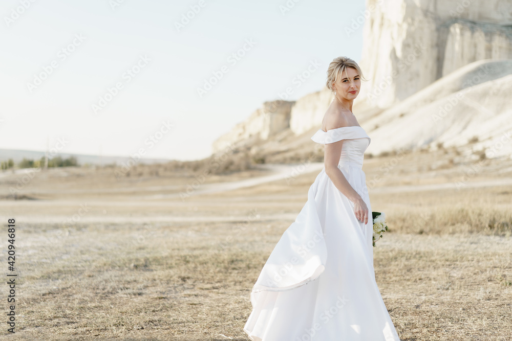 Portrait of a beautiful blonde bride in a white dress with bare shoulders
