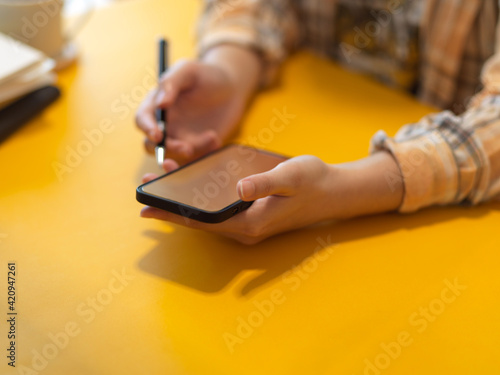 Female freelancer using mock up smartphone in her hands on stylish workspace in home office room