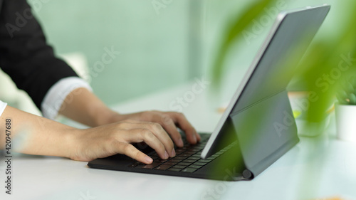 Female hands typing on tablet keyboard on white table decorated with plant pot