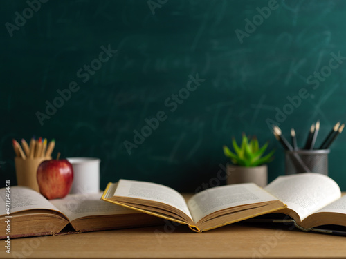 Study table in classroom with opened books, stationery and apple in with blackboard background