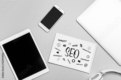 Modern devices with notebook on grey background. Concept of SEO
