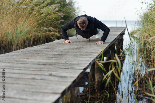Middle-aged man working out doing press-ups on a wooden jetty