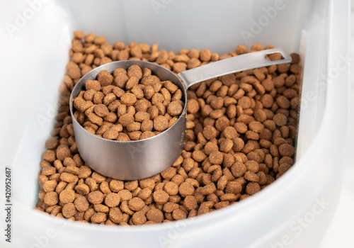 Fotografie Kibbles with measuring cup inside larger food storage bucket
