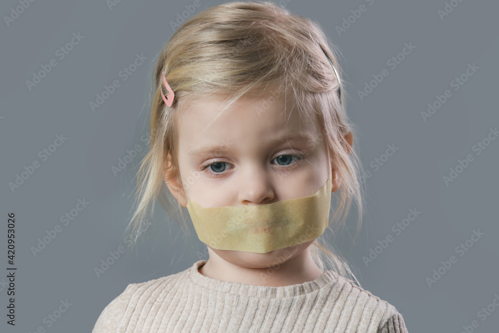 Studio portrait of adorable little girl with adhesive tape over her mouth. Little girl with no