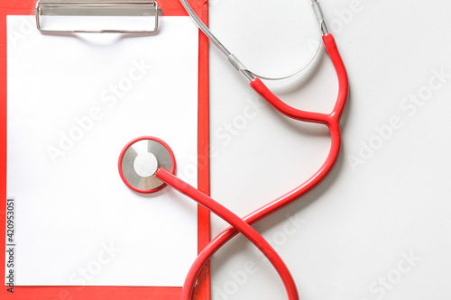 Modern stethoscope and clipboard on light background, closeup