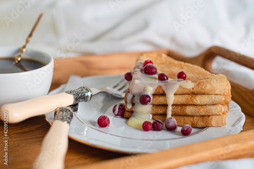 Food tray. Thin pancakes with condensed milk and berries. Romantic breakfast with pancakes and coffee in bed. Copy space