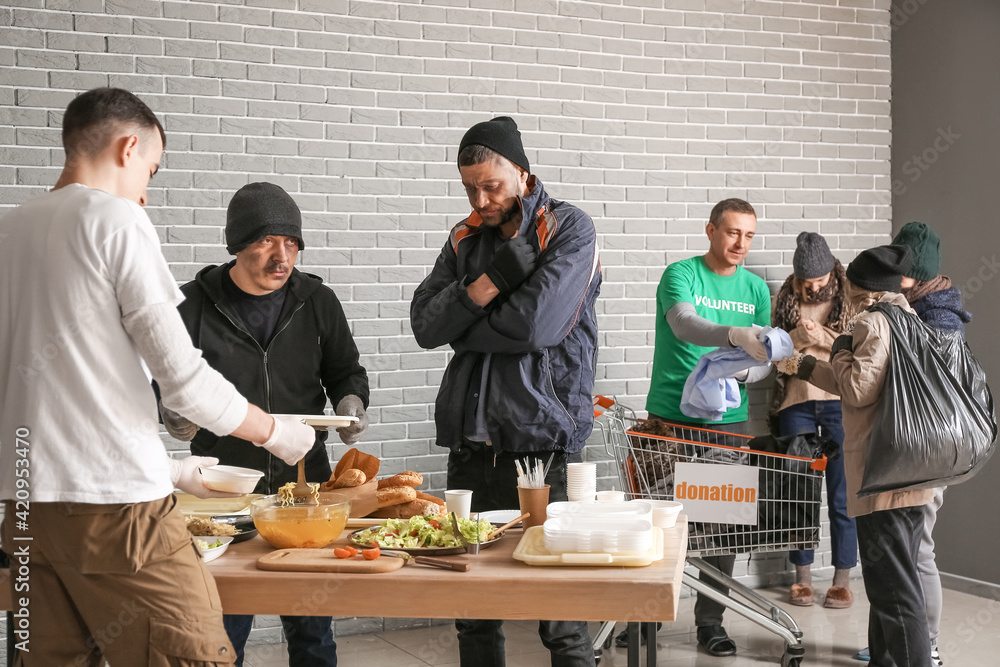Volunteers giving food and clothes to homeless people in warming center ...