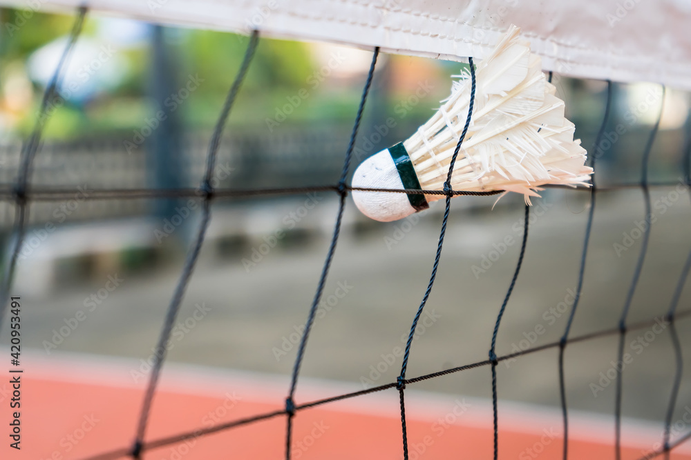 Selective focus of white shuttlecock stuck in the net with blurred background.