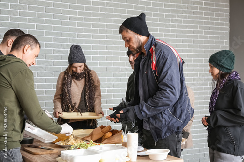 Фотография Volunteers giving food to homeless people in warming center