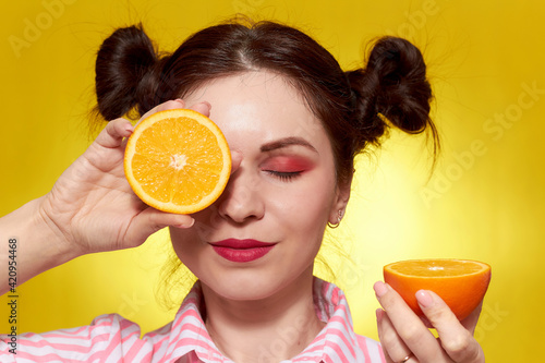 Girl with painted eyes close-up, on a yellow background with an orange. The concept of cosmetology. The yellow background color easily changes to another one.