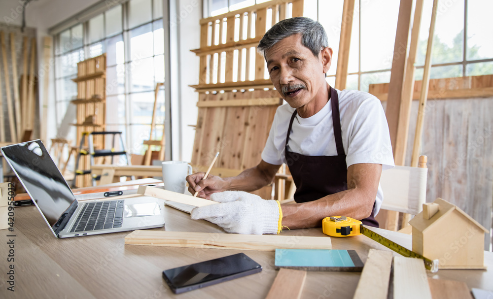 Senior Asian carpenter writing down data from laptop Senior Asian carpenter writing down data from laptop