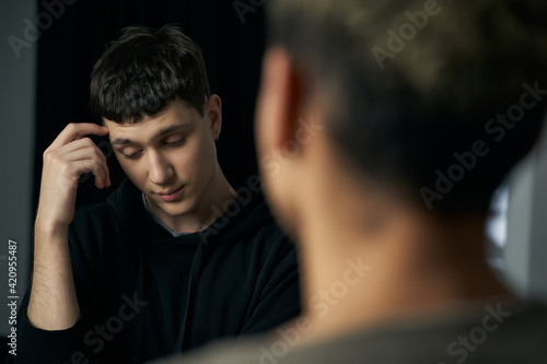 Staged photo illustrates problems and conflicts in gay couple relationships. Moment of showdown: young black-haired man with far-away look is standing in front of his partner and listening to him.  © RedUmbrella&Donkey