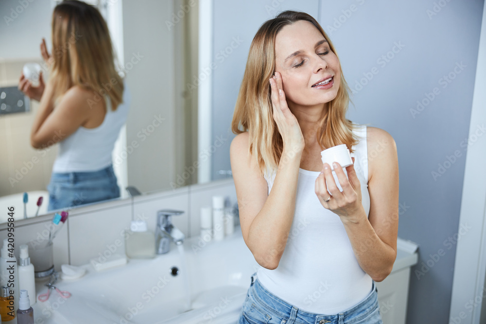Charming woman using face cream in bathroom