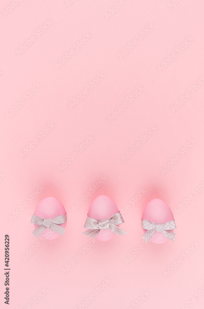 Elegant easter eggs with silver bows in row on pastel pink background, vertical, stories.
