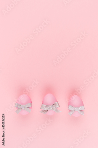 Elegant easter eggs with silver bows in row on pastel pink background, vertical, stories.