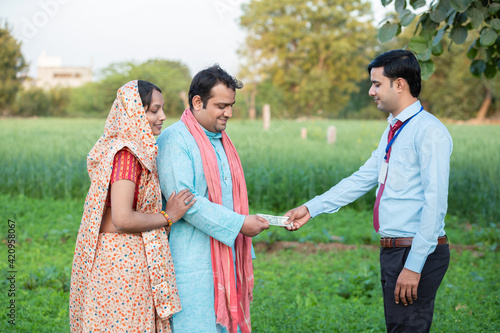 Young rural indian couple farmer receive money from banker at agriculture field. © gajendra