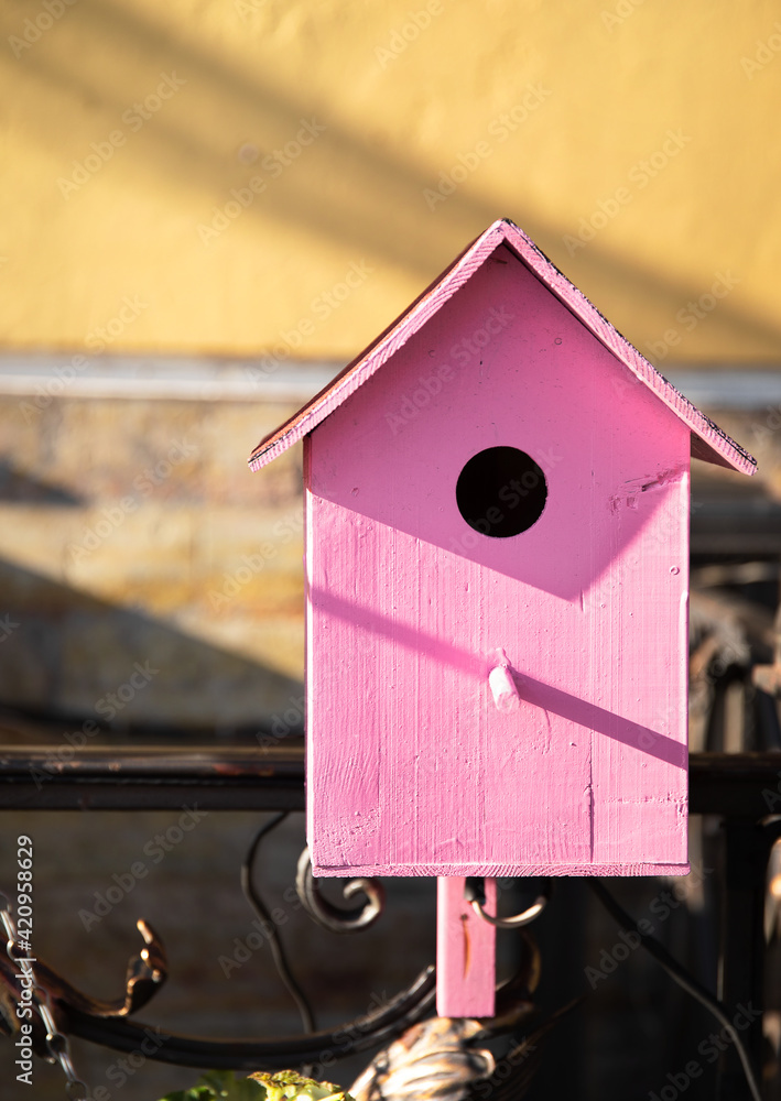 wooden pink birdhouse on a yellow wall background on a sunny bright day. Creative Bird House