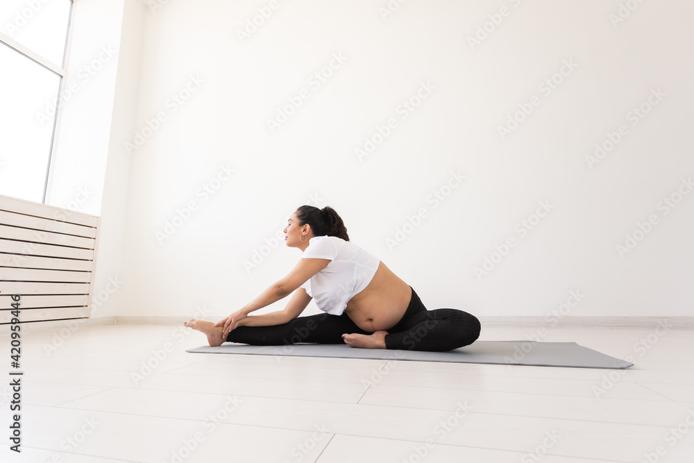 Purposeful pregnant woman exercises during yoga class and relaxes while sitting on a mat on the floor. Concept of physical and mental preparation of the body for childbirth. Place for text Purposeful pregnant woman exercises during yoga class and relaxes while sitting on a mat on the floor. Concept of physical and mental preparation of the body for childbirth. Place for text