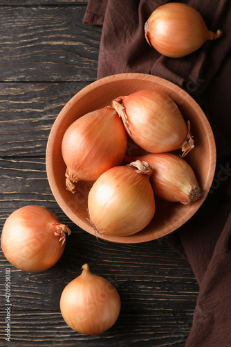 Bowl with fresh onion and kitchen towel on wooden background