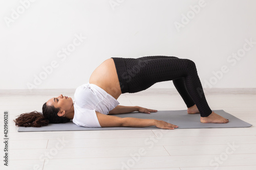 Young flexible pregnant woman doing gymnastics on rug on the floor on white background. The concept of preparing the body for easy childbirth