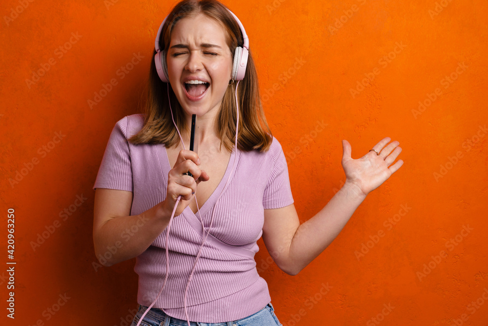 Fototapeta premium Joyful woman singing while listening music with headphones and cellphone