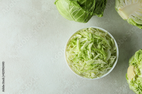 Bowl with sliced cabbage and fresh cabbage on white textured table