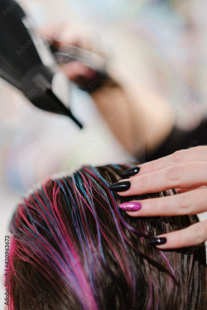 Naklejka premium The hairdresser combs and dries with hairdryer dyed red color hair.