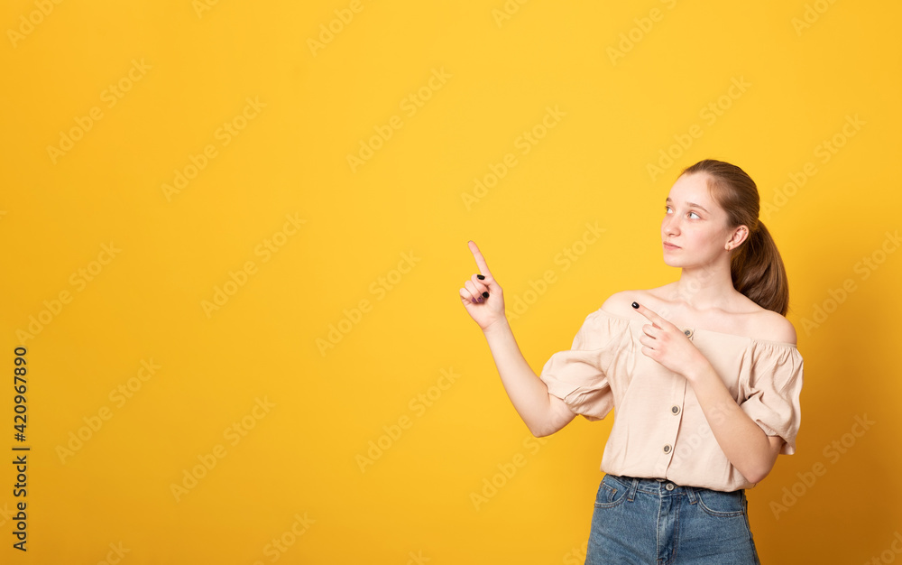 Banner. Smiling girl gives advice and points right, promots product, wears casual t-shirt, poses against yellow background, indicates at advertisement, introduces promo with pleased expression Banner. Smiling girl gives advice and points right, promots product, wears casual t-shirt, poses against yellow background, indicates at advertisement, introduces promo with pleased expression