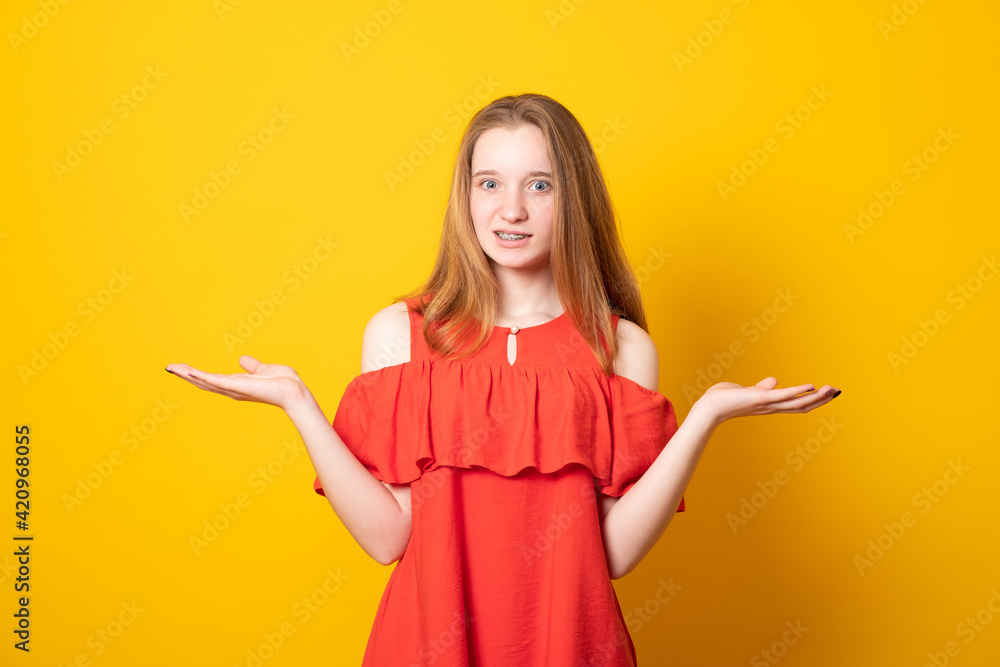 Studio portrait of attractive teenager smile with braces on the teeth shrugging her shoulders having some doubts. Emotional girl being confused while making some decisions. Studio portrait of attractive teenager smile with braces on the teeth shrugging her shoulders having some doubts. Emotional girl being confused while making some decisions.