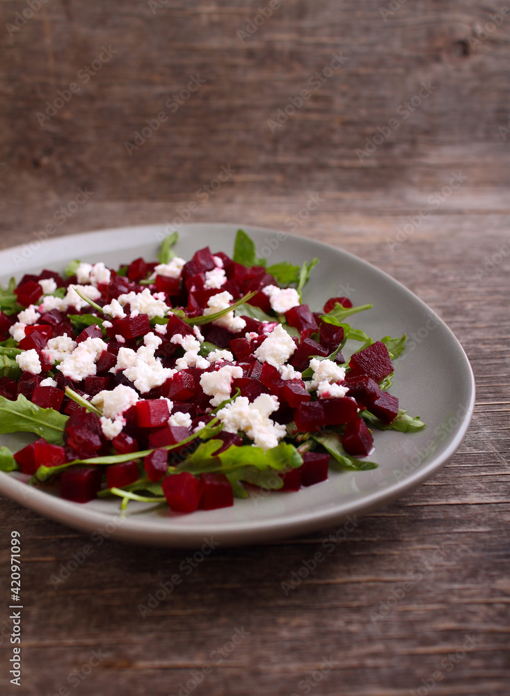 Fresh salad with beetroot, arugula and feta cheese in a plate on a dark background.