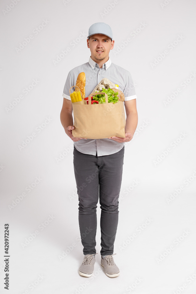 full length portrait of delivery man in uniform holding paper bag full of products over white background full length portrait of delivery man in uniform holding paper bag full of products over white background