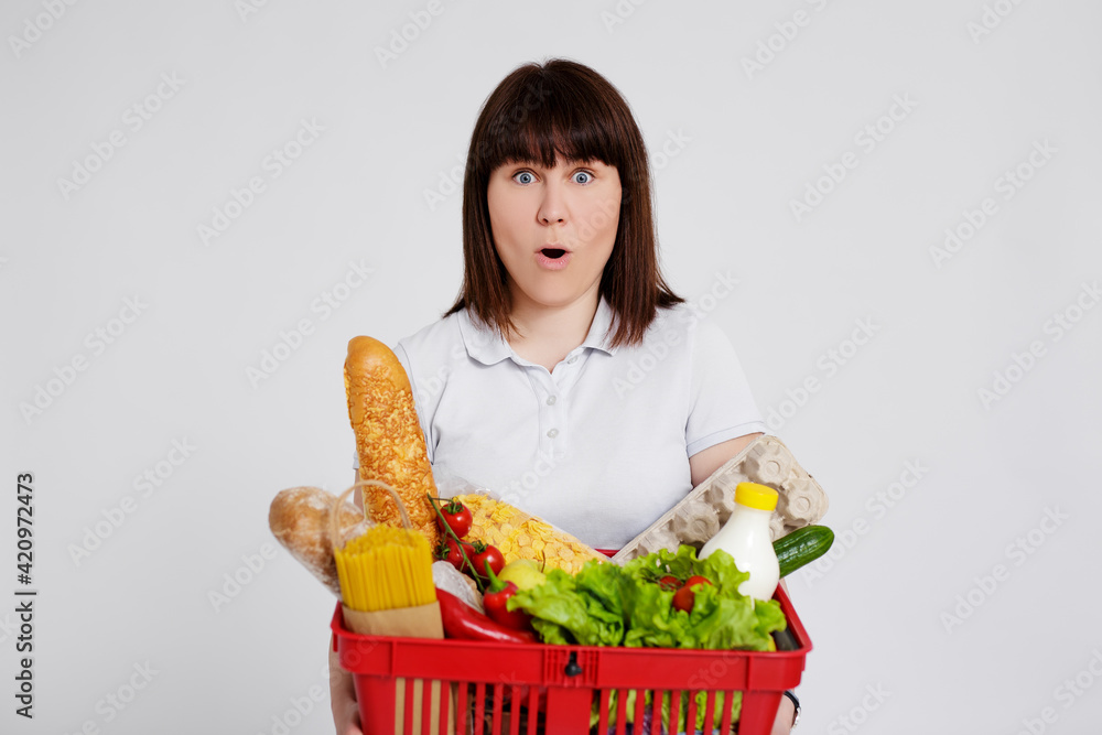 young amazed woman with shopping basket full of products posing over white background young amazed woman with shopping basket full of products posing over white background
