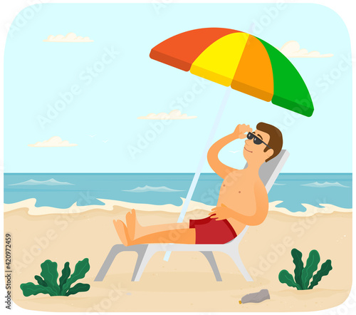 Smiling guy is sitting in sun lounger under umbrella and tanning. Man is sunbathing at resort