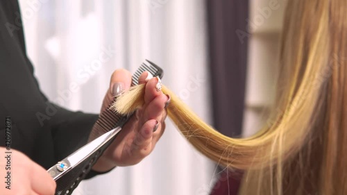 Close-up of a hairdresser hands cutting the ends of a blonde woman hair. Beauty salon. Professional hair care.