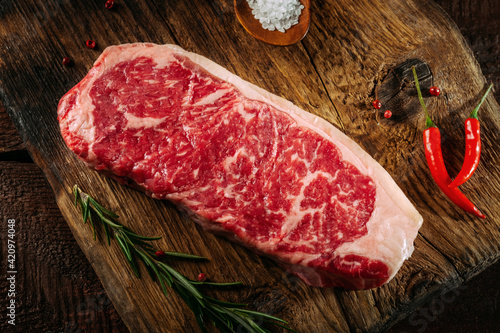 Foto Raw striploin steak of beef on a board with seasonings, salt and red pepper