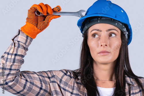 Portrait of a young woman auto mechanic in a hard hat and with a key looking to the side on a white background. photo
